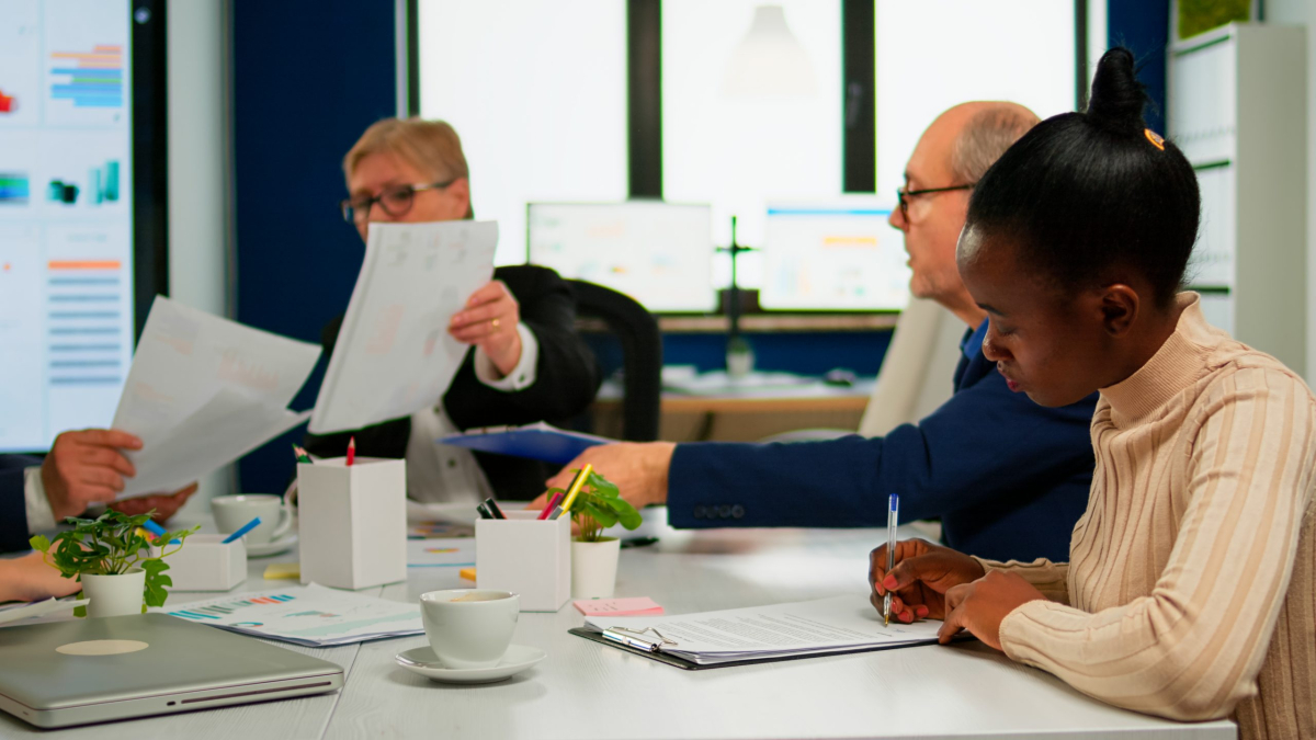 African businesswoman reading documents, signing its while business partners sharing paperwork sitting at conference table in broadroom. Executive director meeting shareholders in start up office